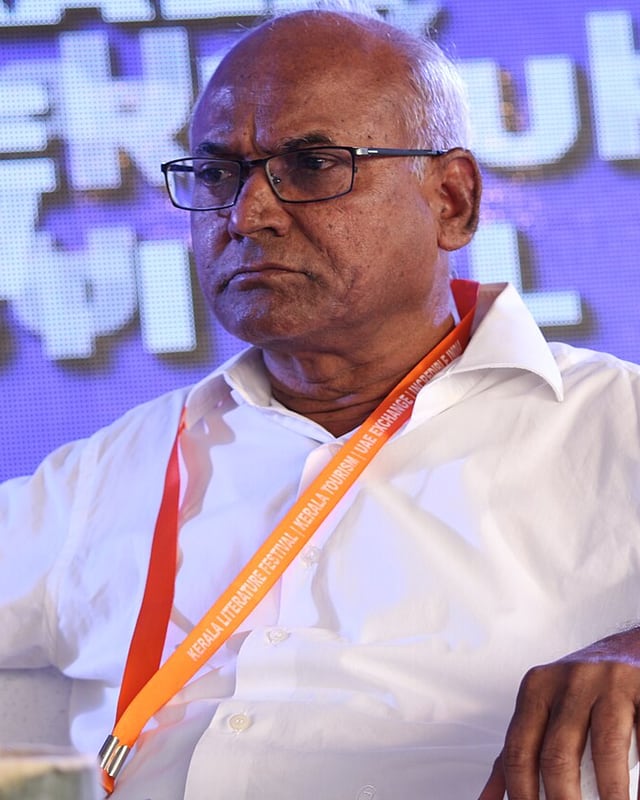 Seated on a literature festival panel in a white shirt, wearing a festival lanyard.