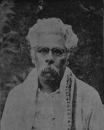A 1924 studio portrait: white hair and beard, round spectacles, and a patterned shawl over one shoulder.